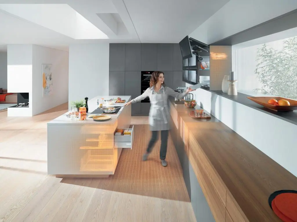 Modern kitchen with person preparing food and use runners and lift systems powered with Servo drive by BLUM