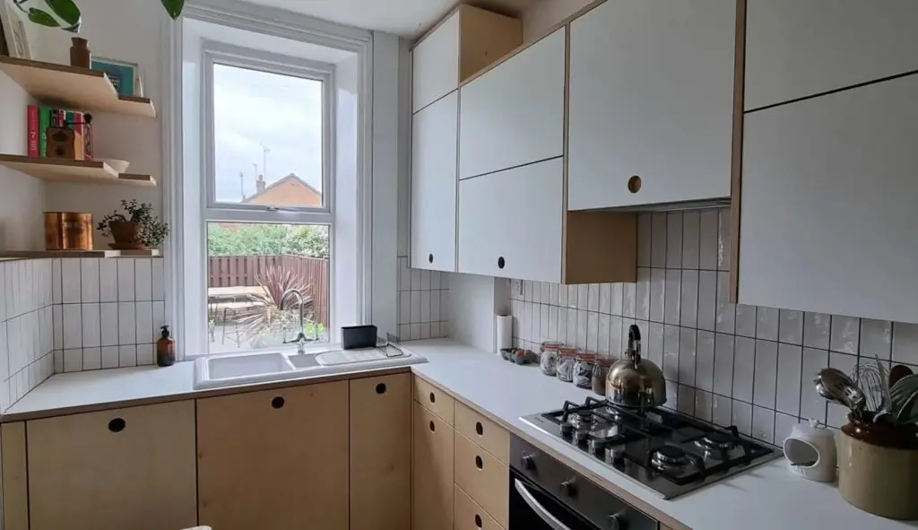 Birch plywood kitchen with exposed ply edges, white laminated upper cabinets, circular finger-pull handles, and tiled splashback, handcrafted by JS DECO.