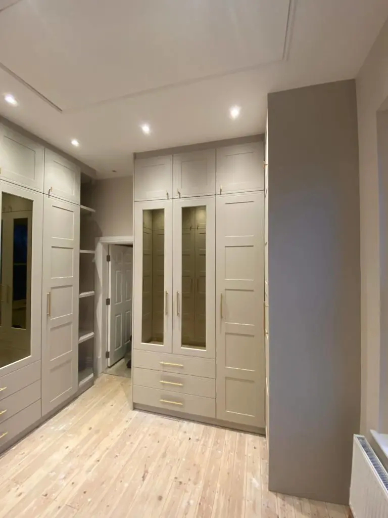 Tall fitted wardrobes around the walk-in room with open shelves beside a doorway