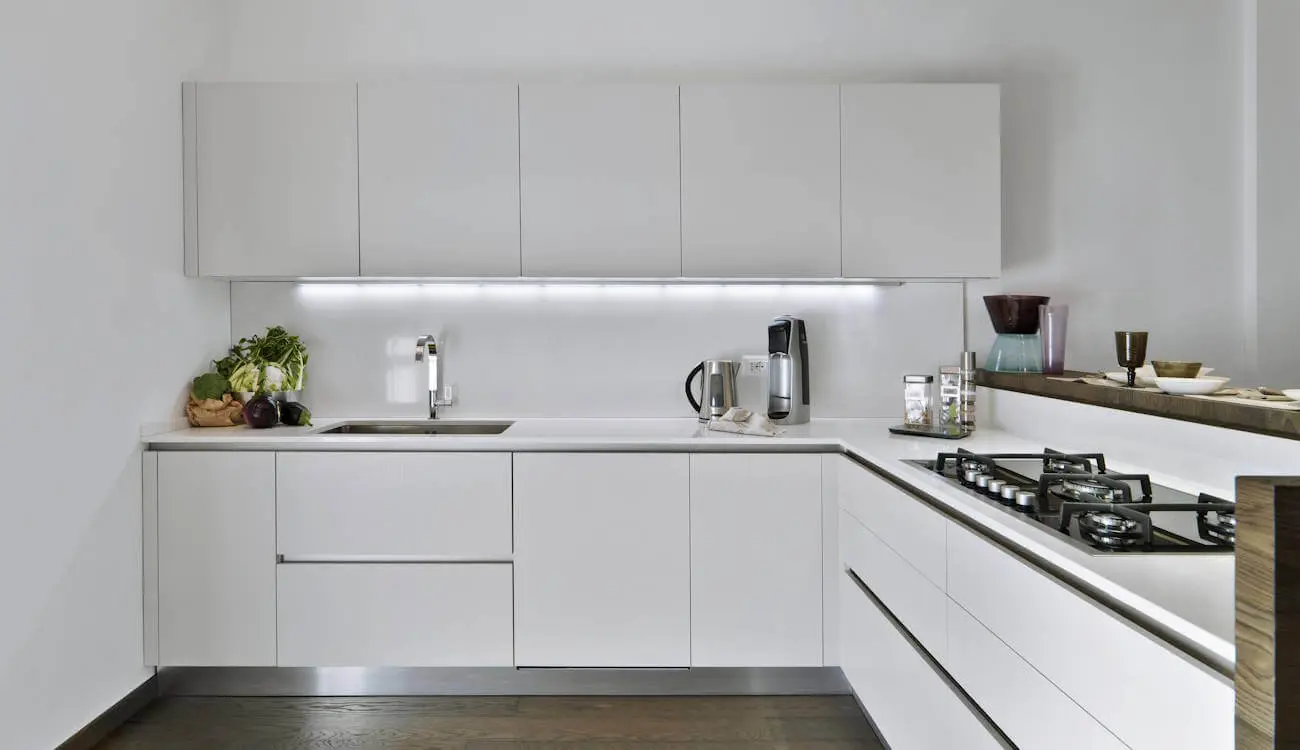 FENIX NTM Bianco Alaska white handleless L-shape kitchen with integrated LED lighting and modern worktop.