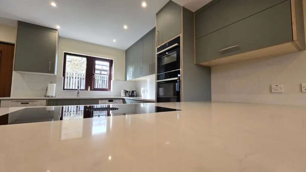 Muted green FENIX cabinetry and a white quartz peninsula in the Verde Kitami kitchen