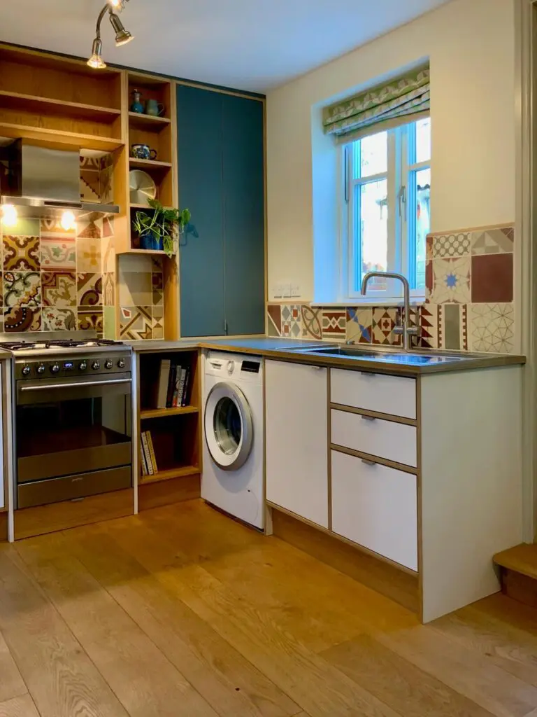 The sink run, with white base cabinets, green worktop and open shelving beside the cooker.