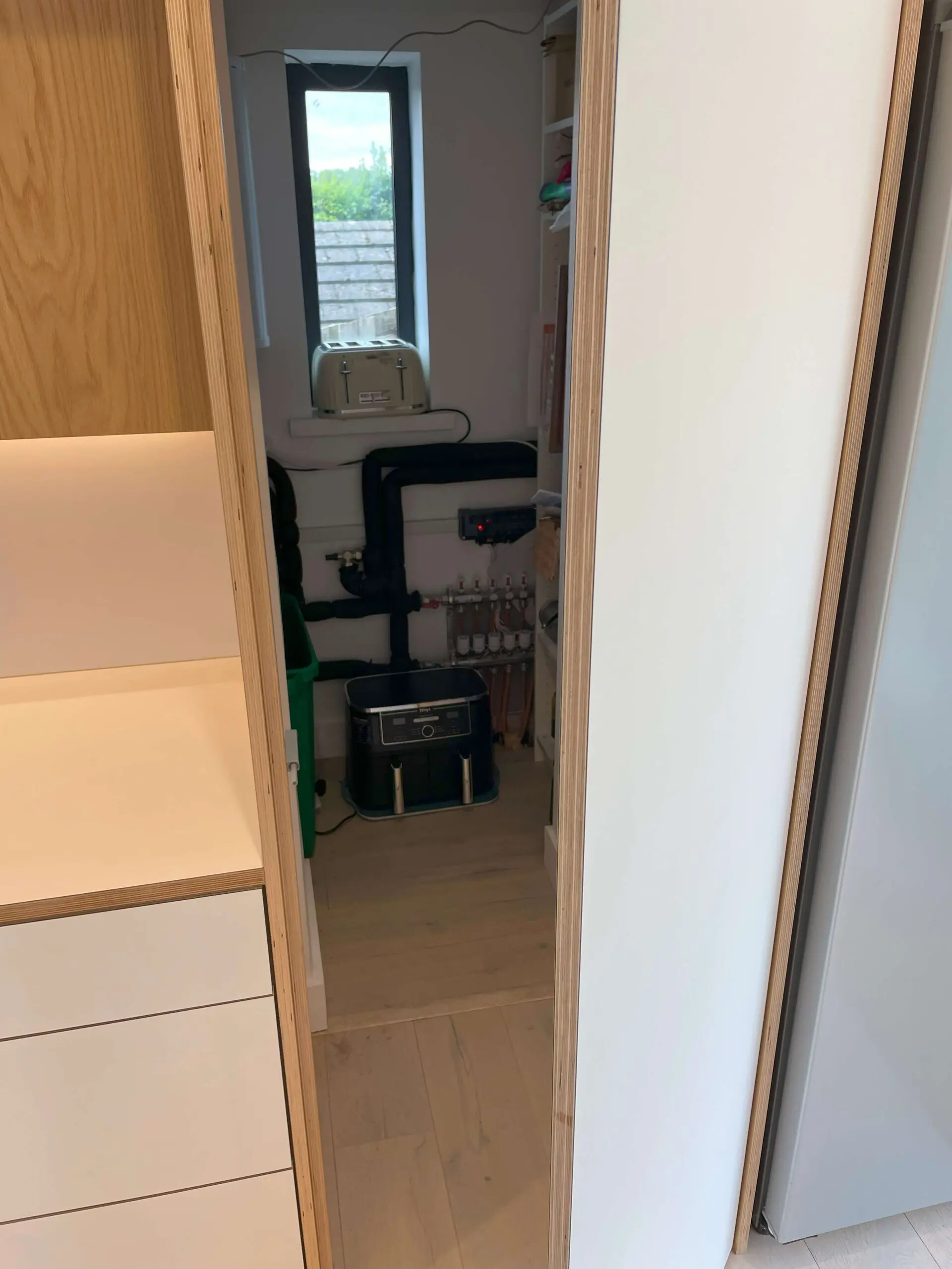 Hidden utility room entrance disguised as oak veneer cabinet in Scandinavian kitchen Bristol by JS DECO