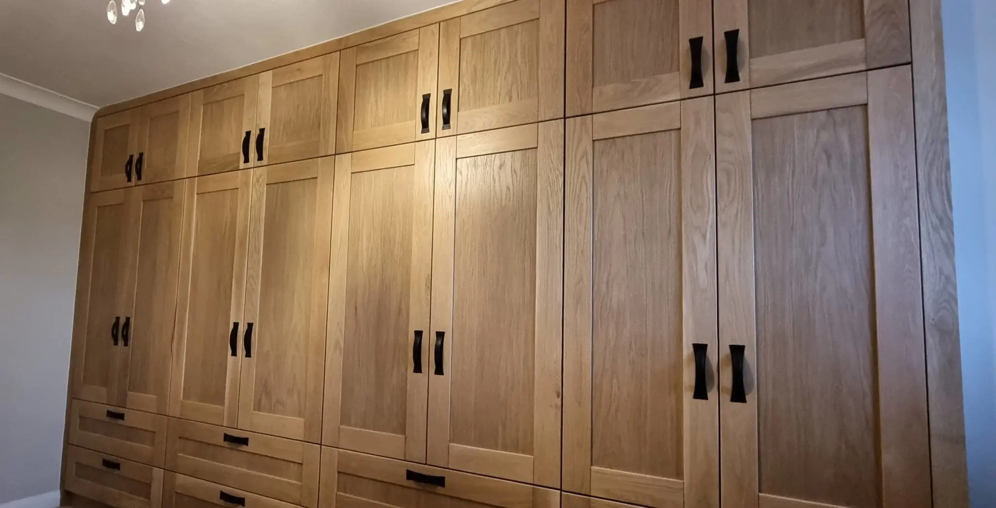 Close-angle view of the bespoke solid oak shaker-style fitted wardrobe by JS DECO, showing door grain and black steel handles.