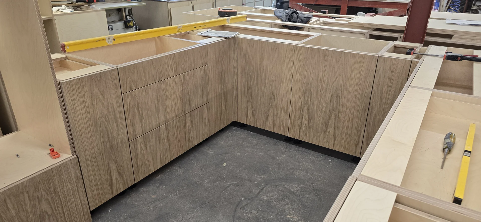 Trial assembly in the JS DECO workshop, showing vertical grain coordinated across a corner run of doors and drawer fronts.