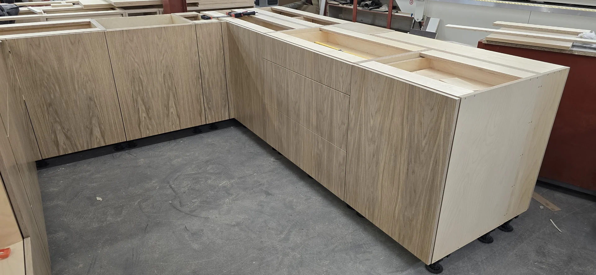 Kitchen fronts during workshop trial assembly, with vertical grain continuing across the stacked drawer fronts and adjacent doors.