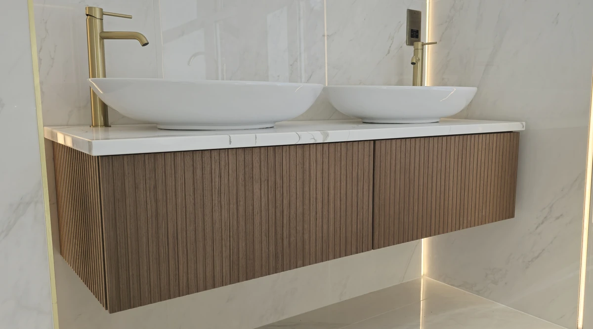 Bespoke wall-mounted vanity with fluted wood fronts, twin basins and brass-coloured taps.