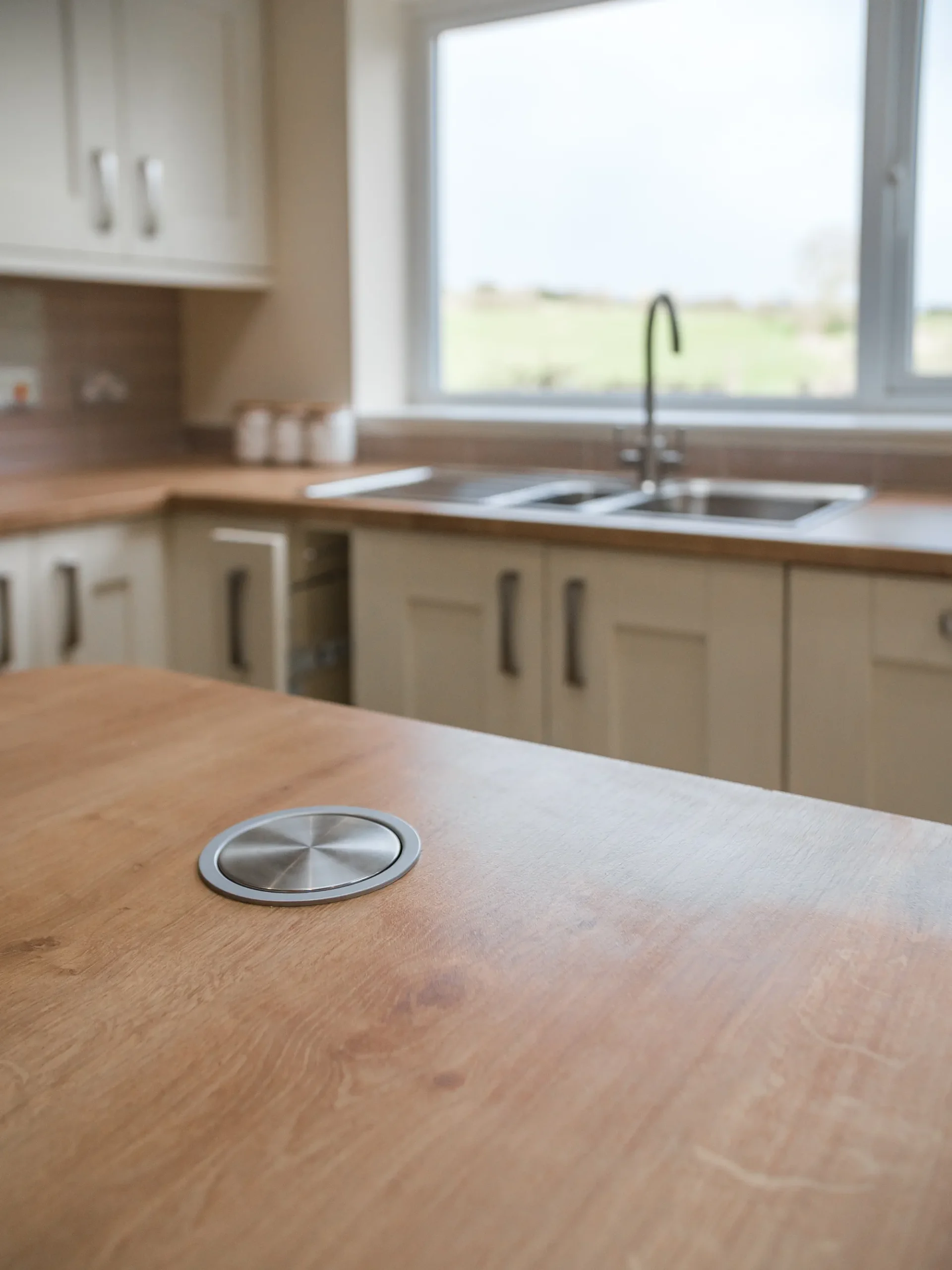 Concealed pop-up power socket set into the oak-effect island worktop. Classic Shaker kitchen with oak-effect island worktop and concealed round socket in Pudsey Leeds.
