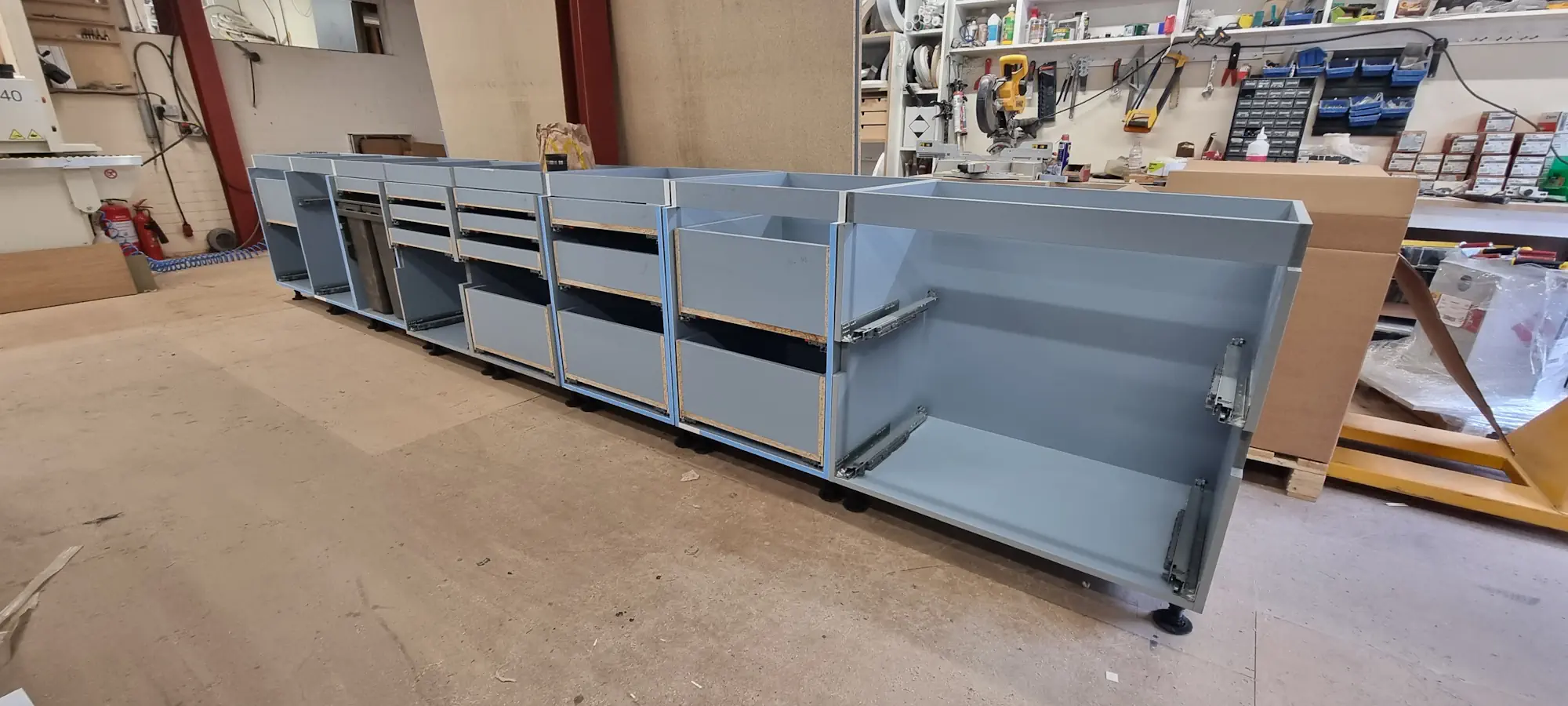 Production stage of white and grey FENIX NTM bespoke kitchen London showing assembled base cabinets and drawer systems in workshop