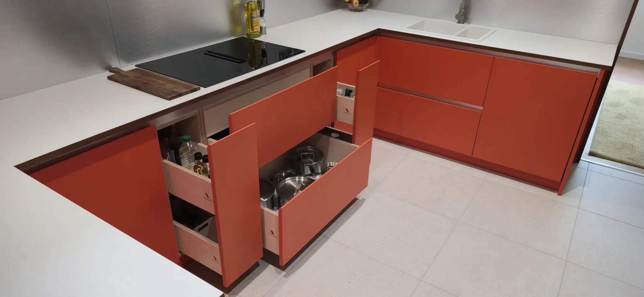 Open drawers and narrow pull-outs beneath and beside the hob reveal the plywood interiors.