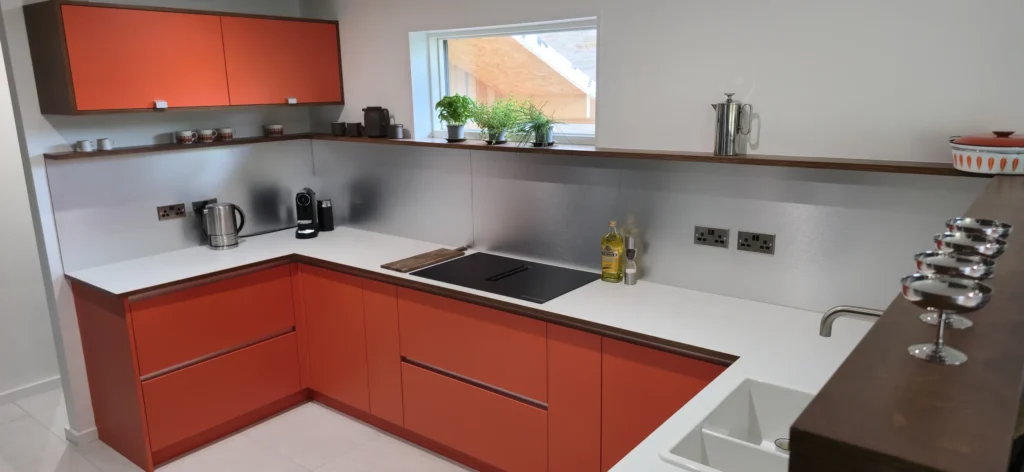 The installed orange kitchen in Cawthorne, with pale worktops, silver-finish splashbacks and a continuous shelf.