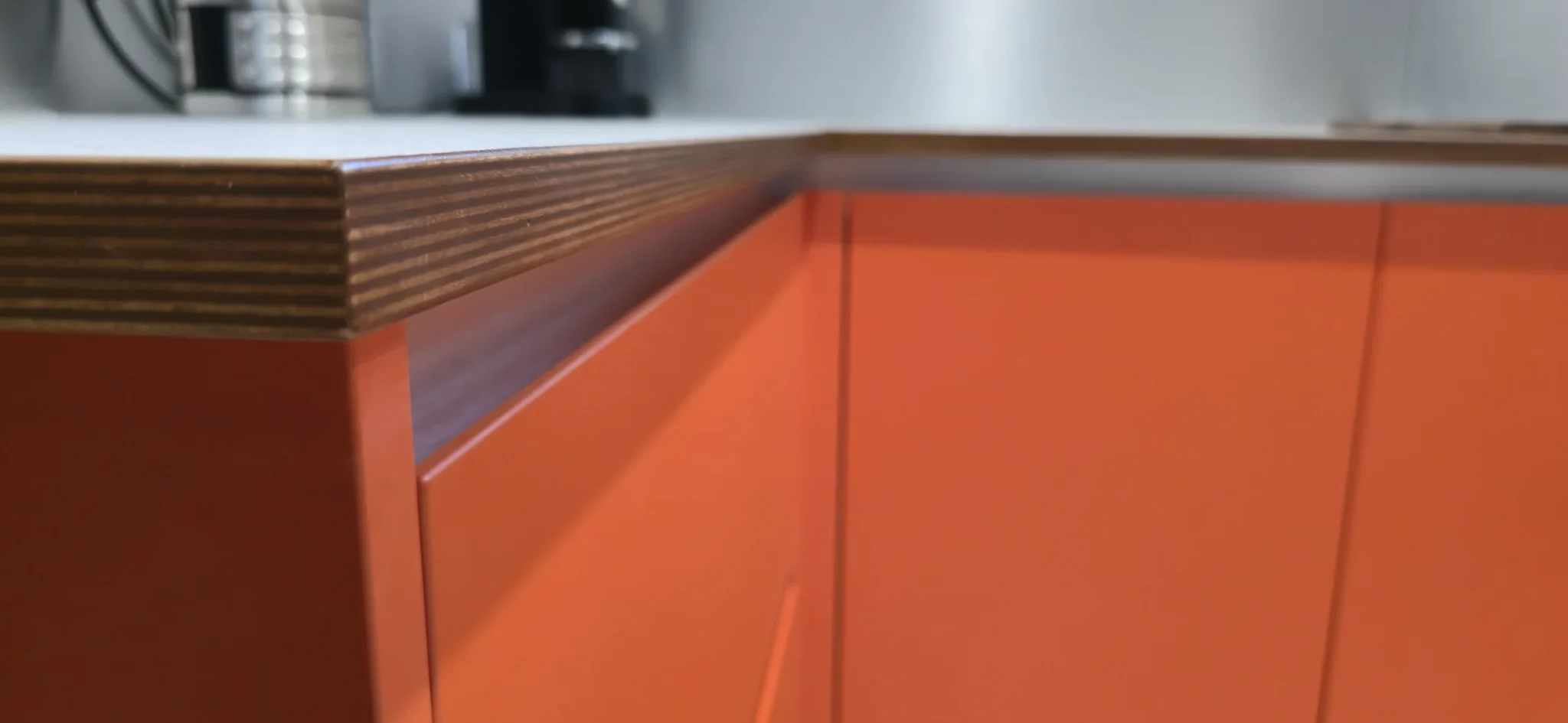 A close view of the layered plywood detail where the worktop and painted cabinetry meet.